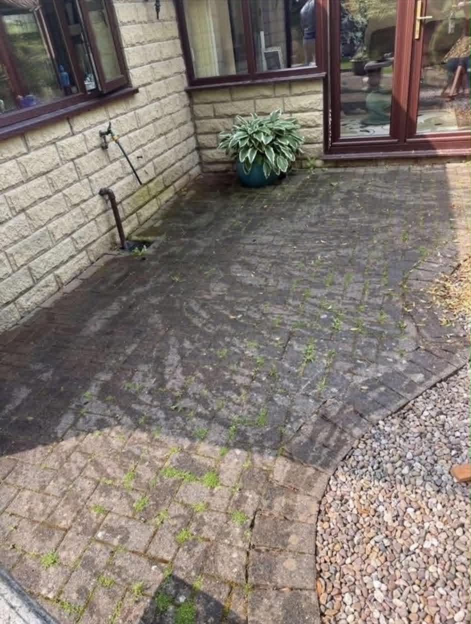 Block paving beside a house, with moss and dirt in the joints
